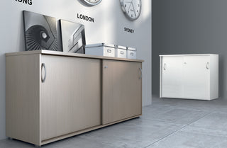 Lifestyle image of a Buronomic Quietude sliding door cabinet in wire oak in a grey showroom