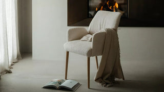 Lifestyle image of a cream Mobitec Enora chair with a throw by a fireplace