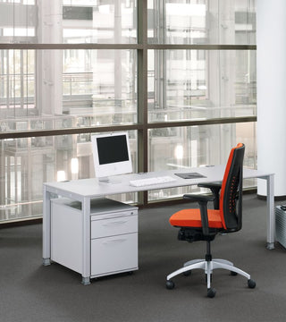 Wit König + Neurath BASIC.4 bureau met ladeblok, monitor en oranje stoel bij een raam